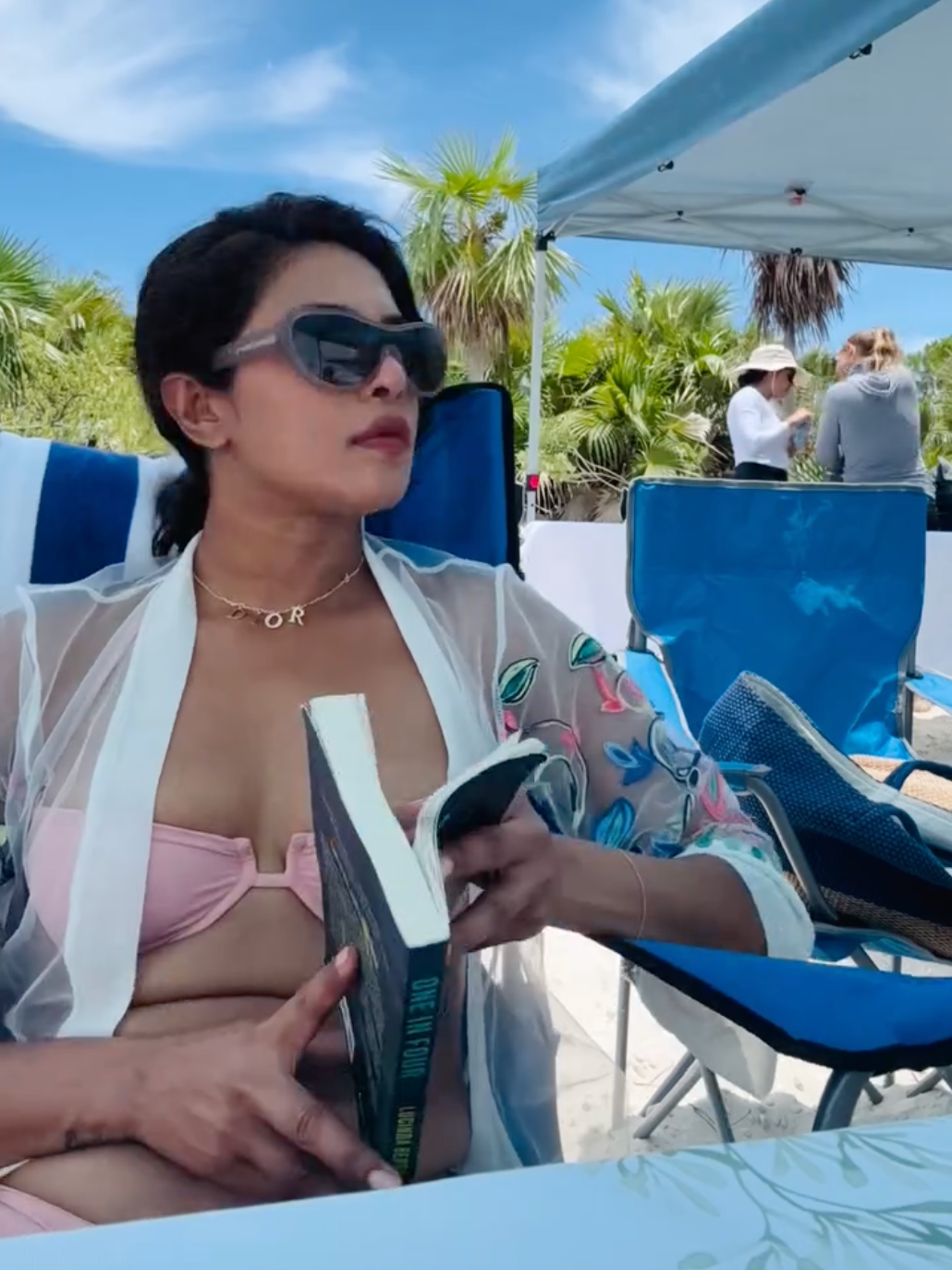 Priyanka Chopra in a bikini reading a book under a blue umbrella on a sunny day.