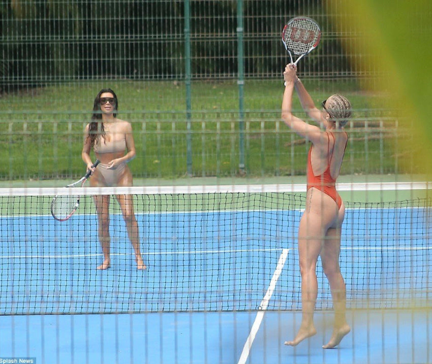 Two women wearing swimwear while playing tennis on a court