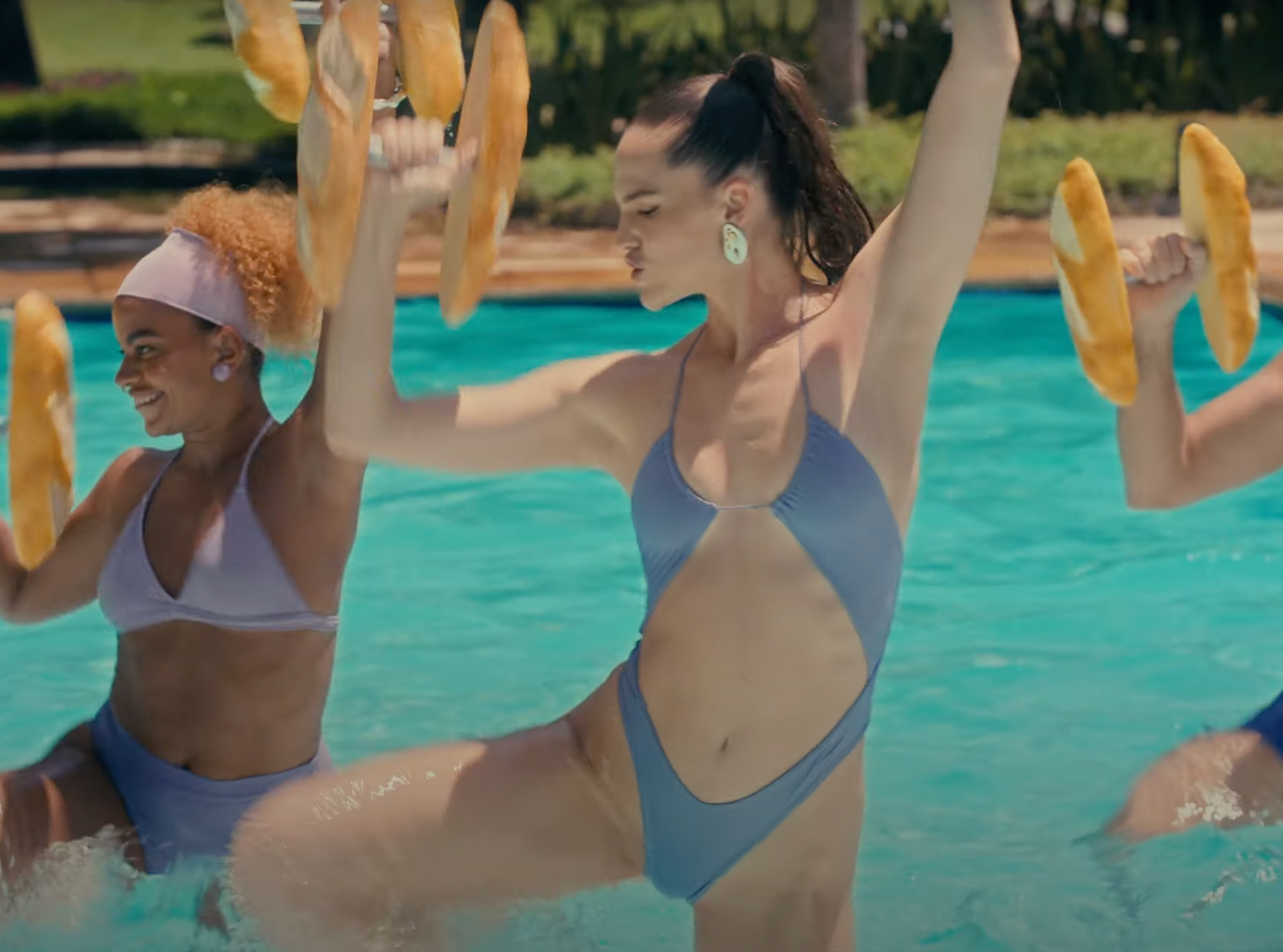 Sofi Tukker wearing a purple one piece with two other women doing water aerobics with weights that look like bread